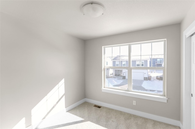 empty room featuring light carpet, visible vents, and baseboards