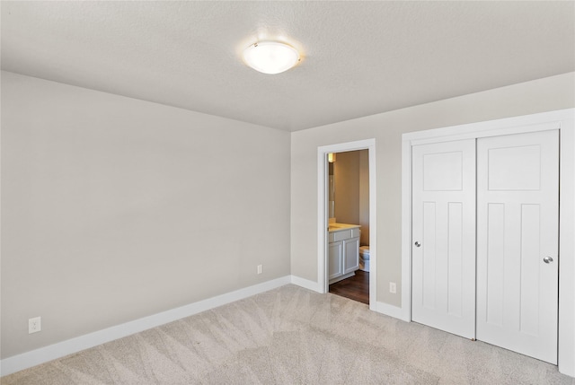 unfurnished bedroom with a textured ceiling, baseboards, a closet, carpet, and ensuite bath