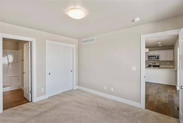 unfurnished bedroom featuring a closet, visible vents, dark carpet, ensuite bath, and baseboards