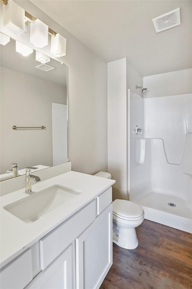 bathroom with visible vents, a shower, toilet, wood finished floors, and vanity