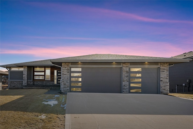 prairie-style home with concrete driveway, stone siding, roof with shingles, and an attached garage