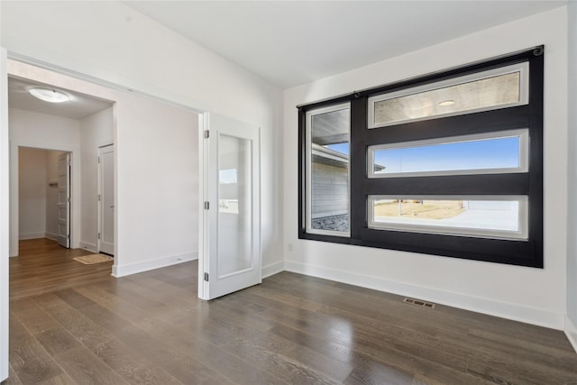 unfurnished room featuring baseboards, visible vents, and dark wood-type flooring