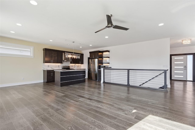 interior space featuring dark wood finished floors, appliances with stainless steel finishes, open floor plan, an island with sink, and dark brown cabinets