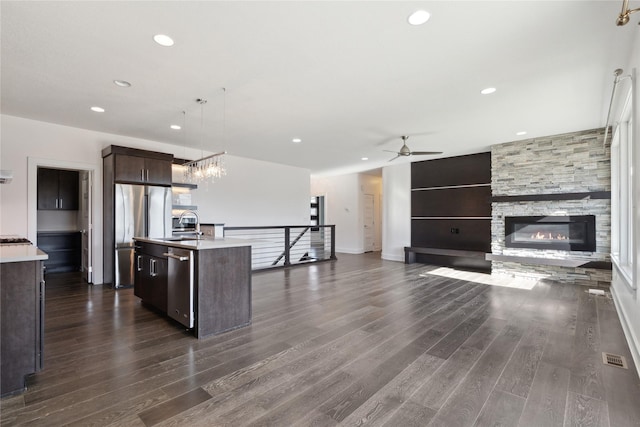 kitchen featuring dark wood-style floors, stainless steel appliances, light countertops, dark brown cabinetry, and an island with sink