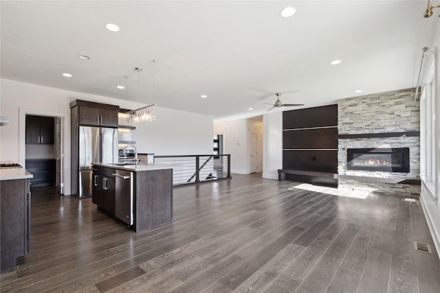 10598 NW 72nd Ln, Johnston, IA 50131 - kitchen with appliances with stainless steel finishes, dark brown cabinetry, a stone fireplace, light countertops, and a center island with sink