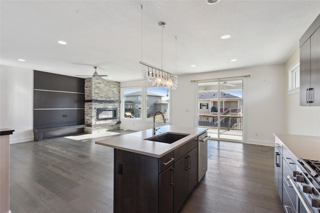 kitchen with a stone fireplace, stainless steel appliances, dark wood-style flooring, a sink, and light countertops