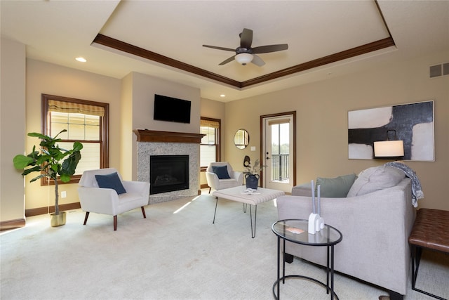 carpeted living area with baseboards, visible vents, a raised ceiling, crown molding, and a fireplace