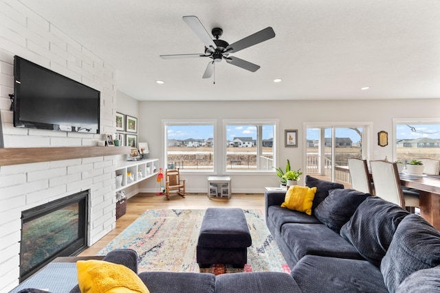 living room with recessed lighting, light wood-style flooring, a ceiling fan, a brick fireplace, and baseboards