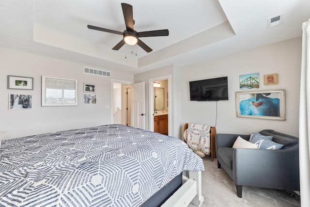 bedroom with a tray ceiling, visible vents, and light carpet