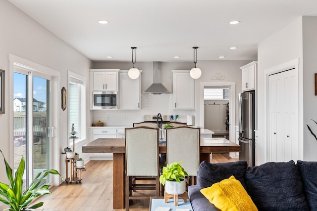 kitchen featuring stainless steel appliances, backsplash, light wood-style floors, white cabinetry, and wall chimney range hood