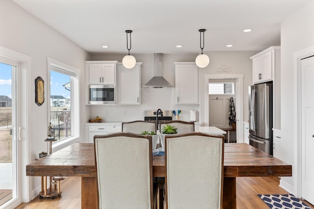 kitchen featuring wall chimney range hood, light wood-style floors, appliances with stainless steel finishes, and white cabinets