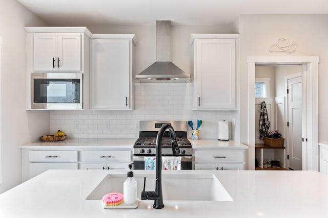 kitchen featuring stainless steel appliances, wall chimney range hood, white cabinetry, and tasteful backsplash