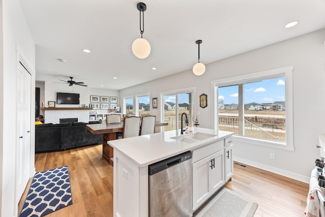 kitchen featuring hanging light fixtures, stainless steel dishwasher, white cabinetry, a sink, and light wood-type flooring