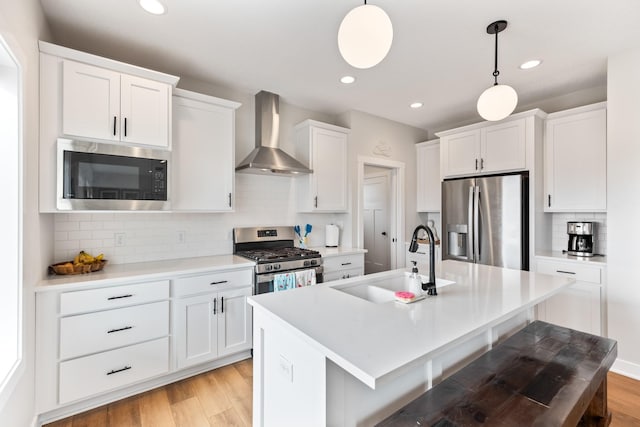 kitchen featuring stainless steel appliances, light wood-type flooring, a sink, and wall chimney exhaust hood