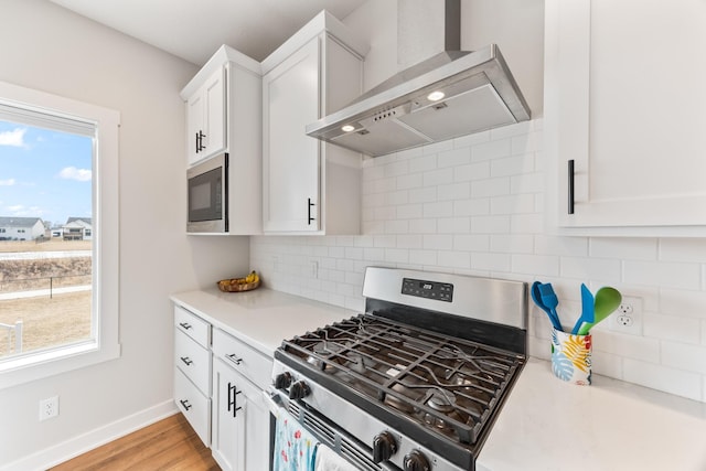 kitchen featuring light countertops, wall chimney range hood, a wealth of natural light, built in microwave, and gas stove