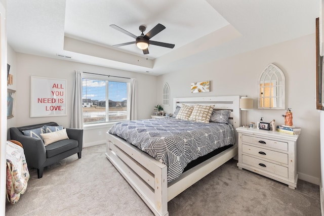 bedroom featuring light carpet, a tray ceiling, visible vents, and baseboards