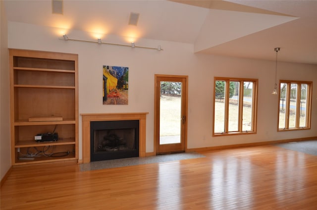 unfurnished living room with a fireplace with flush hearth, wood finished floors, baseboards, and built in shelves