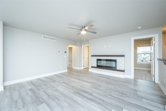 unfurnished living room with light wood-style floors, a glass covered fireplace, visible vents, and baseboards