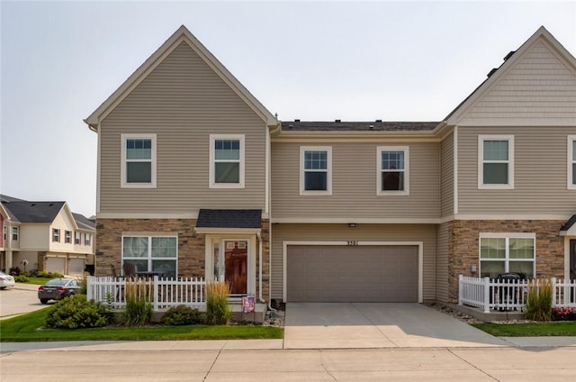 townhome / multi-family property featuring a garage, driveway, stone siding, and fence