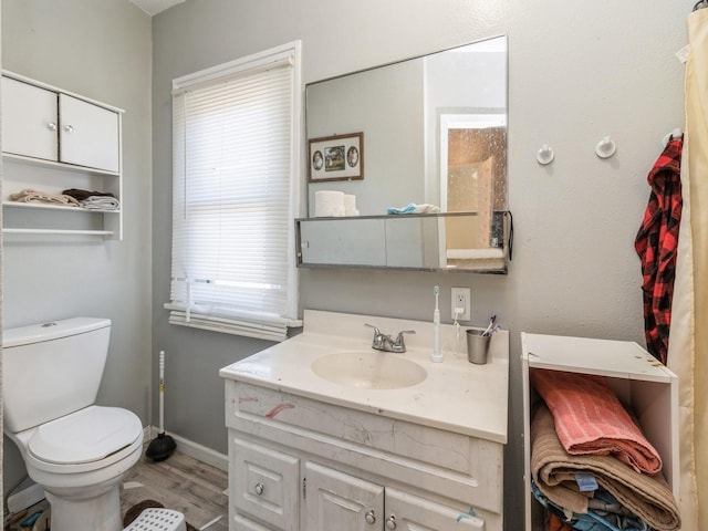 bathroom with toilet, vanity, baseboards, and wood finished floors