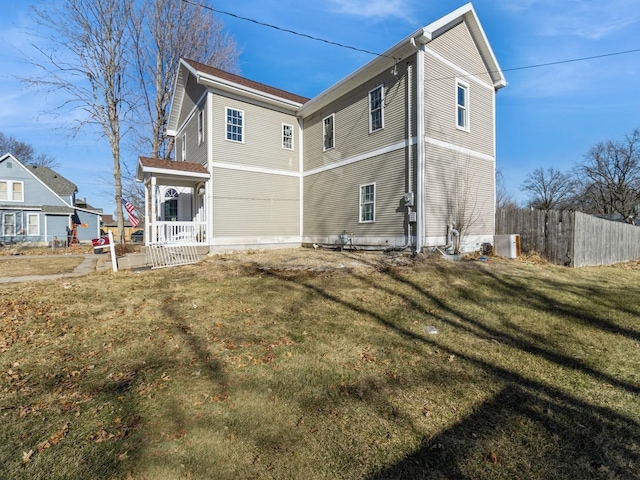 back of house featuring covered porch, fence, and a lawn