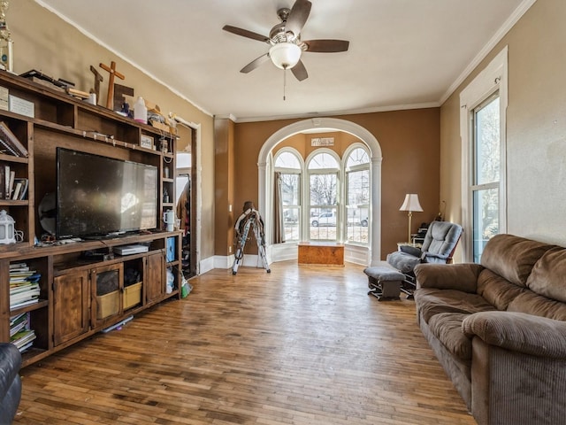 living room featuring baseboards, crown molding, a ceiling fan, and wood-type flooring