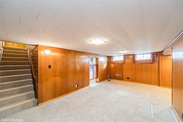 basement with carpet floors, wood walls, stairway, and baseboards