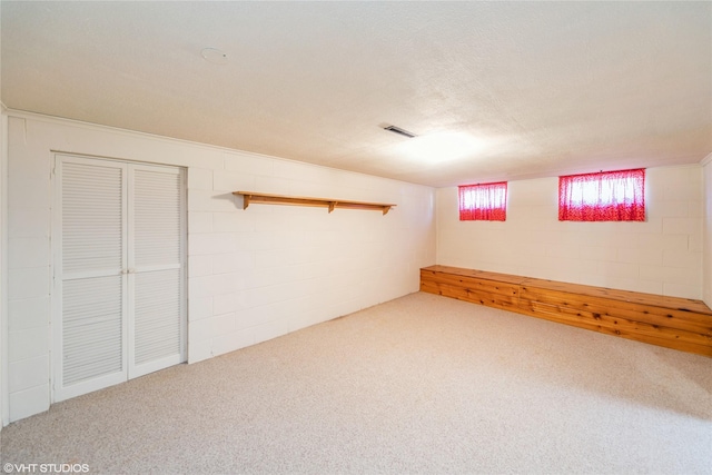 basement with a textured ceiling, carpet floors, visible vents, and concrete block wall