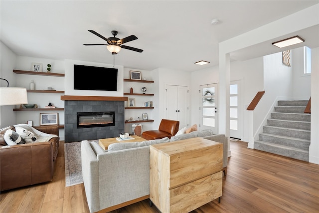 living area featuring stairs, wood finished floors, a tile fireplace, and a healthy amount of sunlight