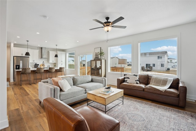 living area featuring baseboards, light wood-type flooring, a ceiling fan, and recessed lighting