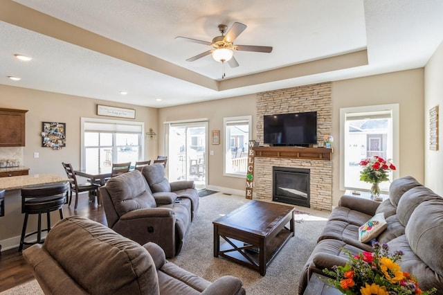 living area featuring dark wood-style floors, a tray ceiling, a fireplace, and baseboards