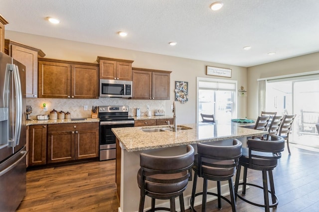 kitchen featuring dark wood-type flooring, a sink, appliances with stainless steel finishes, decorative backsplash, and light stone countertops