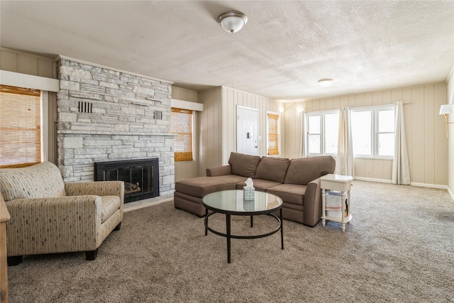 living room featuring carpet floors, baseboards, a textured ceiling, and a stone fireplace