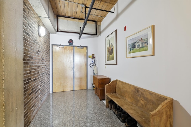 corridor with wood ceiling, brick wall, and speckled floor