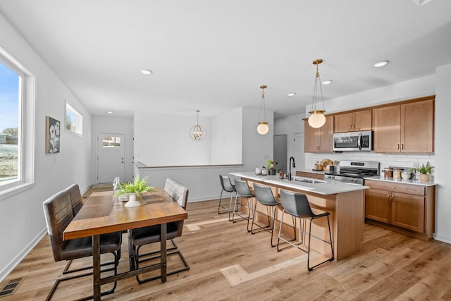 kitchen with a breakfast bar area, tasteful backsplash, appliances with stainless steel finishes, a sink, and light wood-type flooring