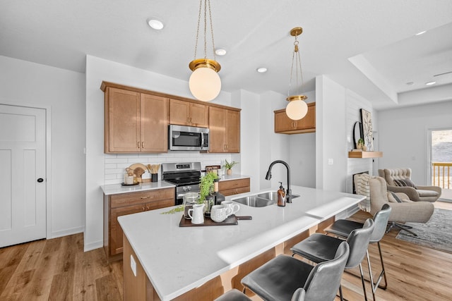 kitchen featuring light wood-style flooring, stainless steel appliances, a sink, backsplash, and brown cabinets