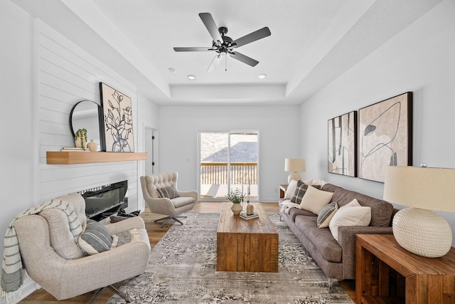 living area featuring ceiling fan, recessed lighting, a glass covered fireplace, wood finished floors, and a raised ceiling