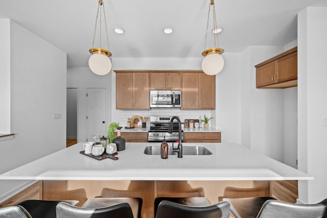 kitchen featuring a sink, light countertops, appliances with stainless steel finishes, brown cabinets, and tasteful backsplash