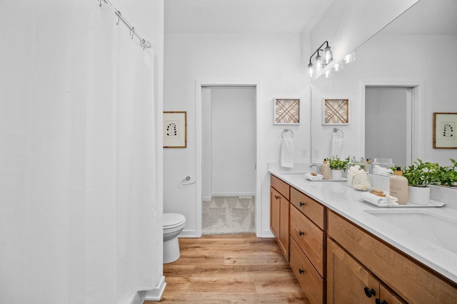 full bath with double vanity, baseboards, toilet, wood finished floors, and a sink