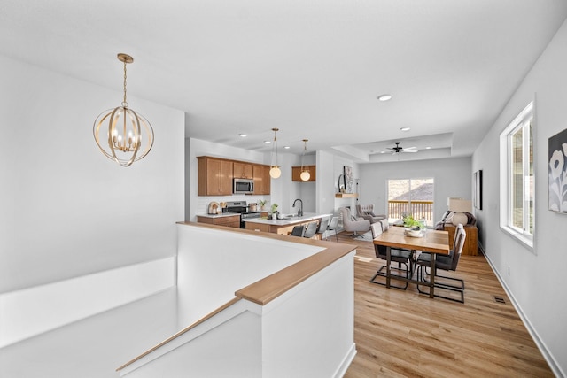 kitchen with a tray ceiling, decorative light fixtures, light wood finished floors, light countertops, and appliances with stainless steel finishes