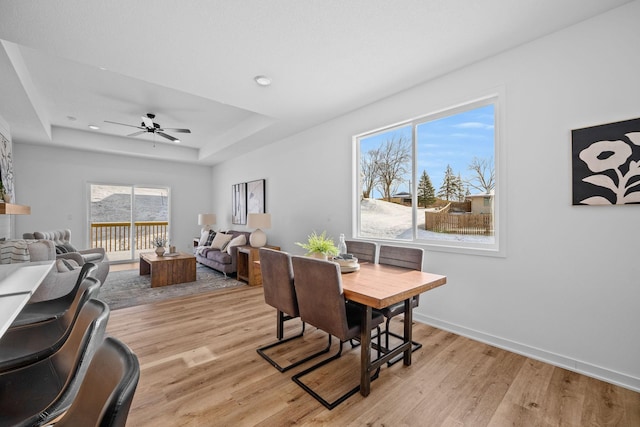 dining area featuring a ceiling fan, light wood-type flooring, a raised ceiling, and baseboards