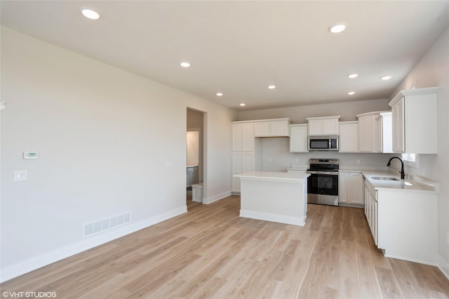2908 Yordi Dr, Norwalk, IA 50211 - kitchen featuring stainless steel appliances, a sink, a center island, light wood-type flooring, and white cabinets
