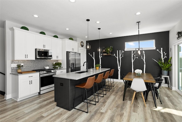 kitchen with an island with sink, a breakfast bar area, appliances with stainless steel finishes, white cabinetry, and a sink