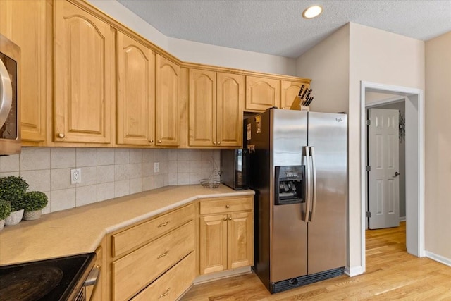 kitchen with light wood finished floors, appliances with stainless steel finishes, light countertops, light brown cabinetry, and backsplash