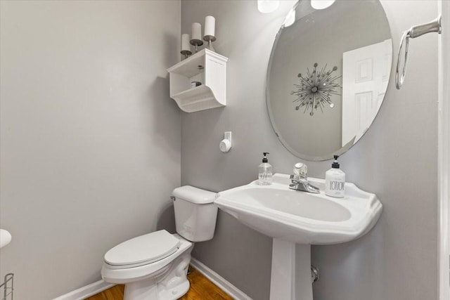 half bath featuring wood finished floors, toilet, and baseboards