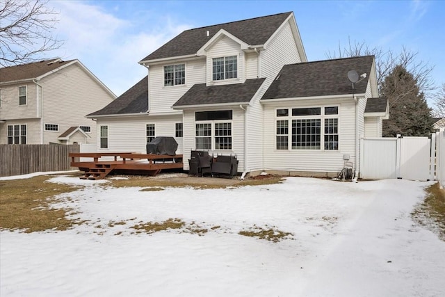 snow covered property with roof with shingles, fence, and a wooden deck