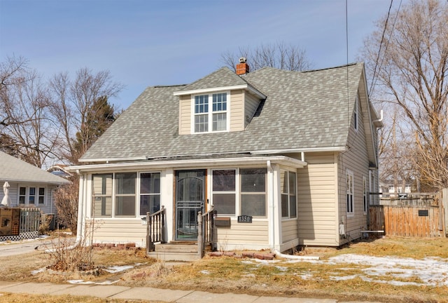 view of front of house featuring a sunroom, a shingled roof, a chimney, and fence