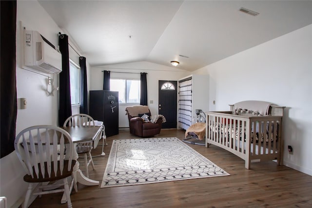 bedroom with visible vents, lofted ceiling, wood finished floors, a nursery area, and a wall mounted AC