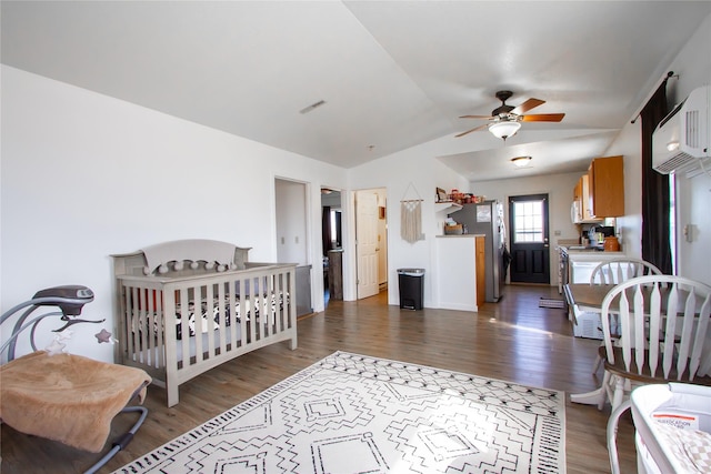 bedroom with wood finished floors, visible vents, vaulted ceiling, freestanding refrigerator, and a wall mounted air conditioner