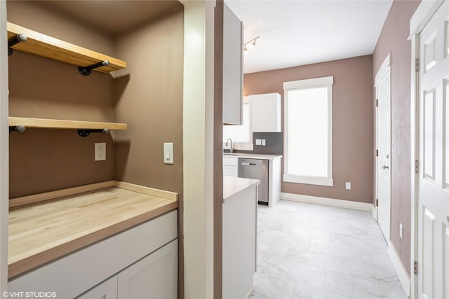 kitchen with a sink, white cabinetry, baseboards, marble finish floor, and stainless steel dishwasher